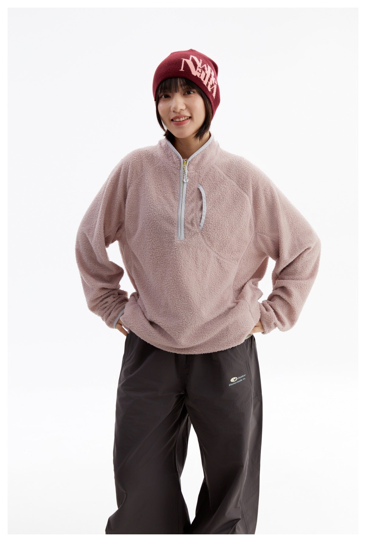Front view of a model in a dusty pink fleece pullover with a short zip and curved chest pocket.