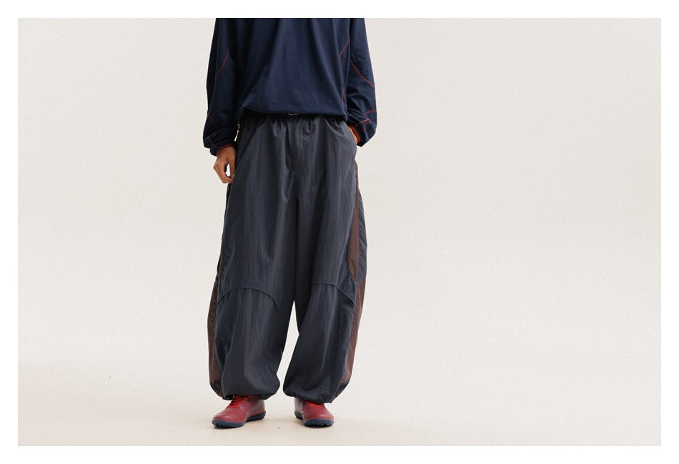 Front view of a model wearing loose charcoal pants with brown side panels and gathered ankles.
