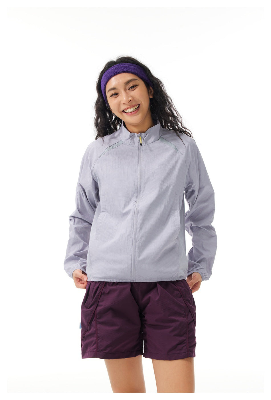 Closer front view of a model wearing a light lavender zip-up jacket and plum shorts.
