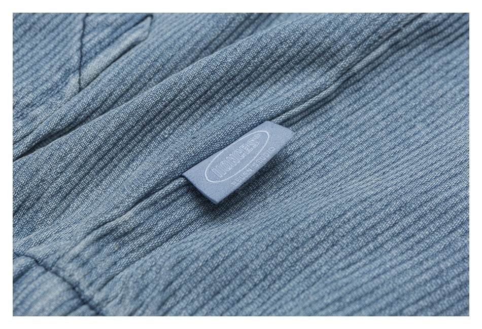 Blue-gray ribbed fabric close-up with a small sewn label bearing an outlined logo.