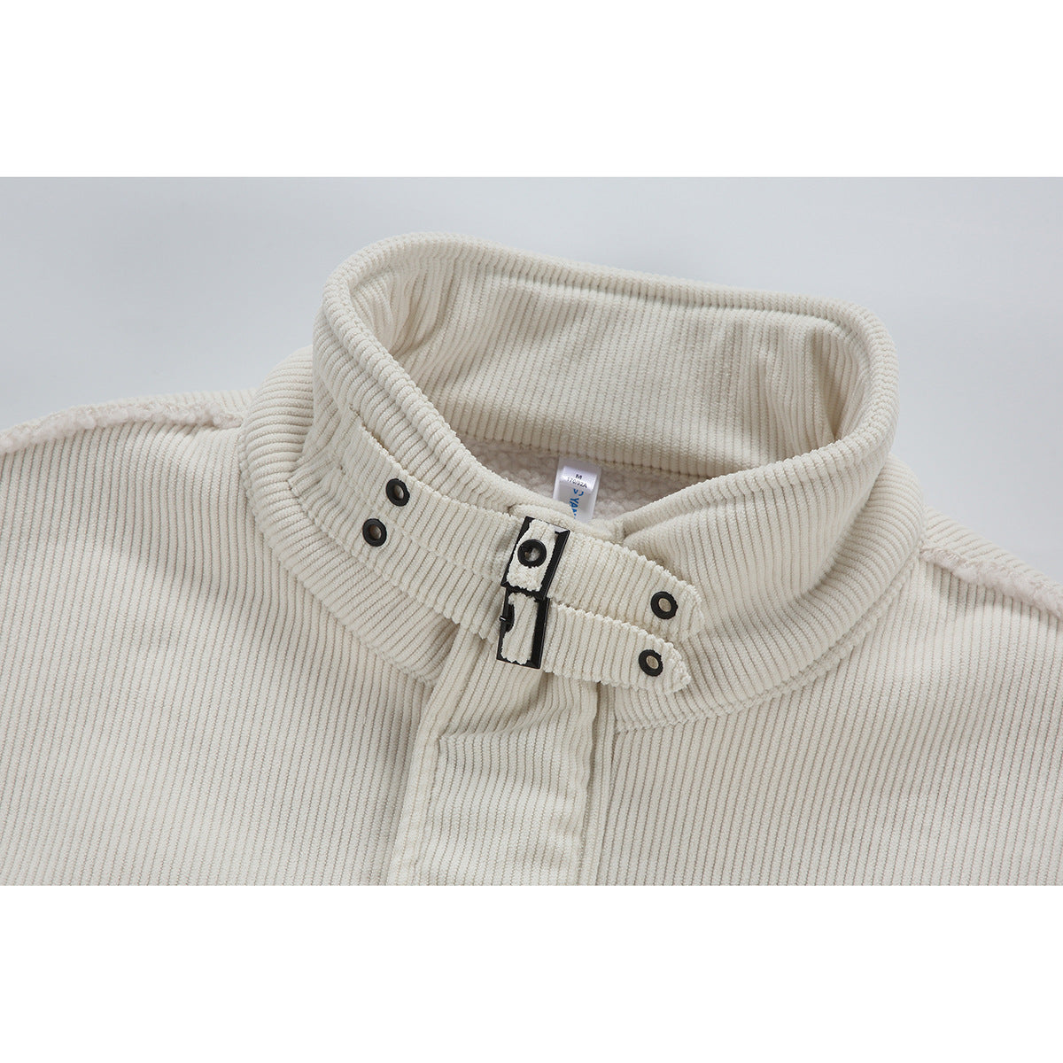 Close-up of an ivory corduroy jacket collar with black snap details and a central buckle closure.