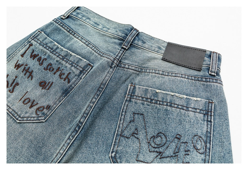 Close-up of the back of blue jeans with two pockets, stitched lettering and a plain dark waistband patch.