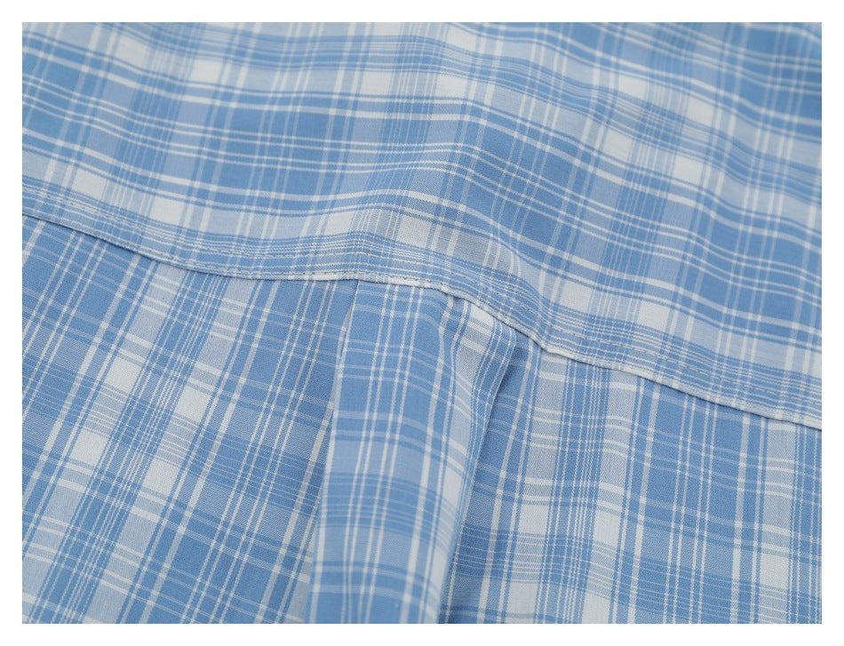 Close-up of blue and white plaid fabric with a curved stitched seam and overlapping folds.