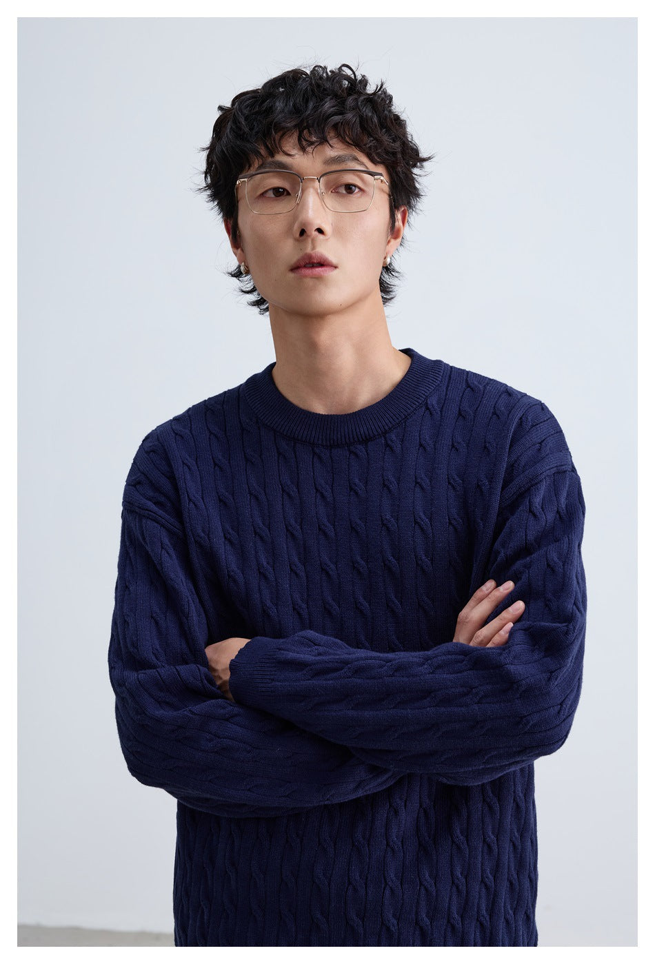 Close view of a model wearing a navy cable-knit crewneck sweater.