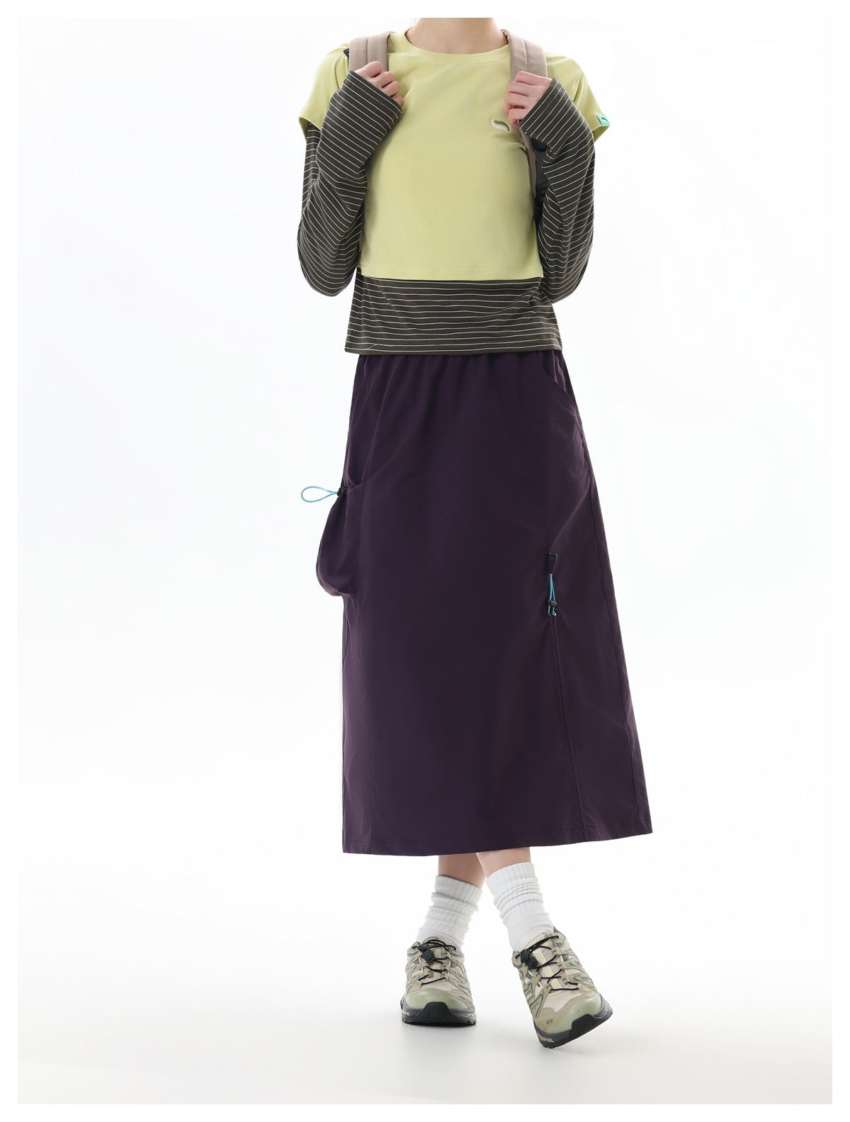 Model wearing a dark plum midi skirt with utility pockets and drawcords, paired with a pale yellow top and striped sleeves.