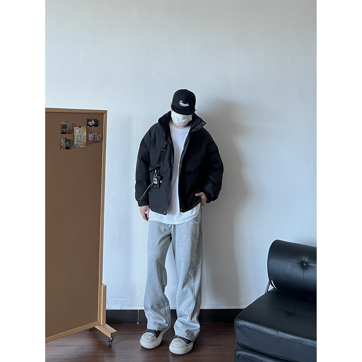 Model wearing a black padded jacket open over a white shirt, with a crossbody strap and pouch.