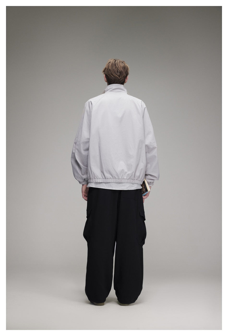 Rear view of a model wearing a light gray jacket with elastic cuffs and hem over black cargo pants.