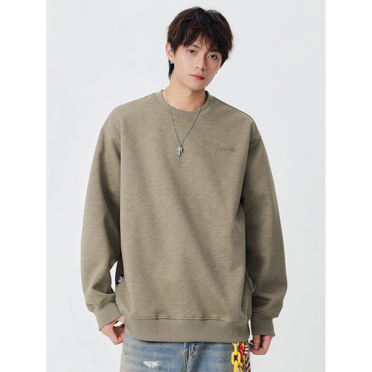 Front view of a model wearing an oversized taupe crewneck sweatshirt with ribbed trim and a small chest logo.