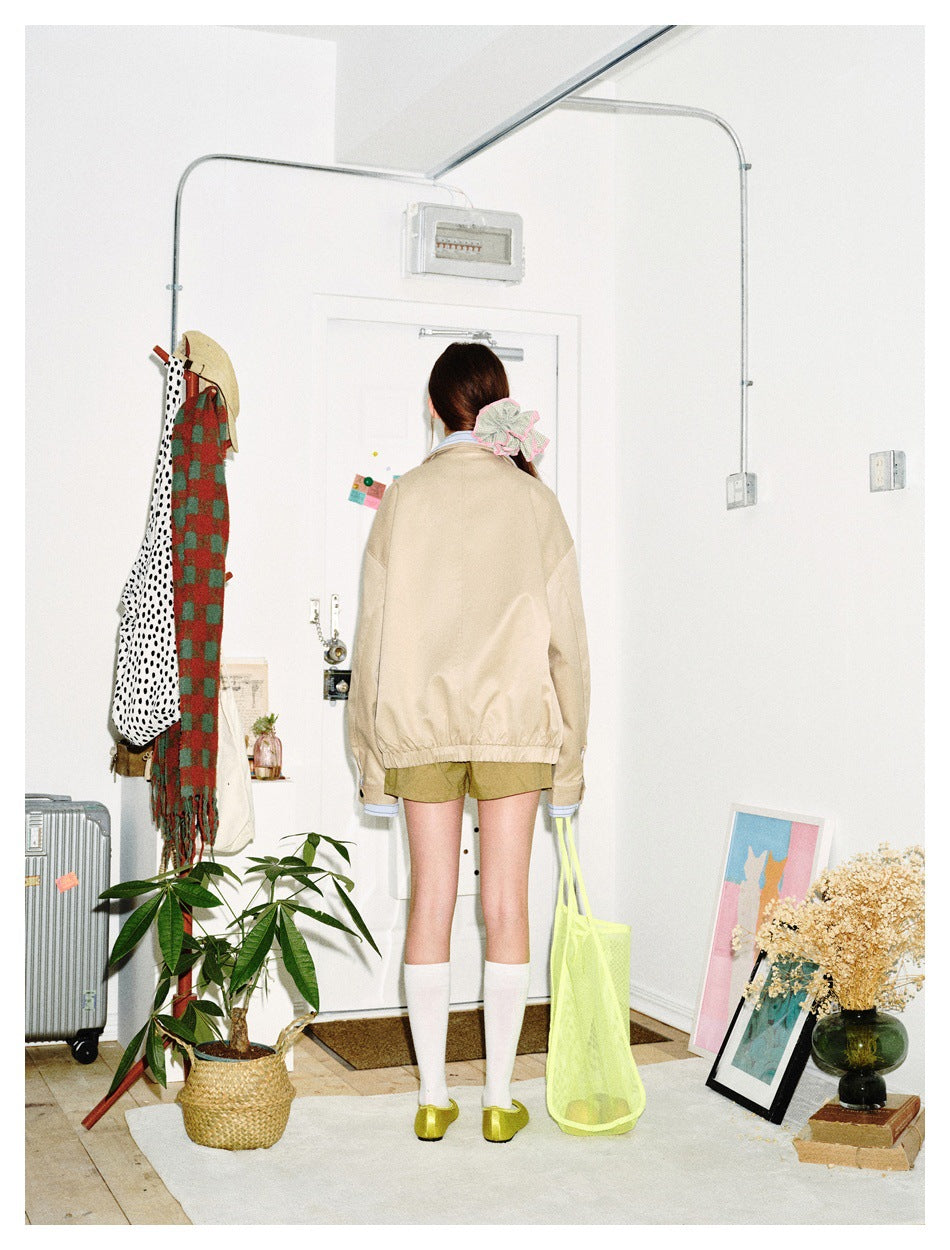 Back view of a model wearing a beige jacket with an elastic hem and striped blue cuffs.