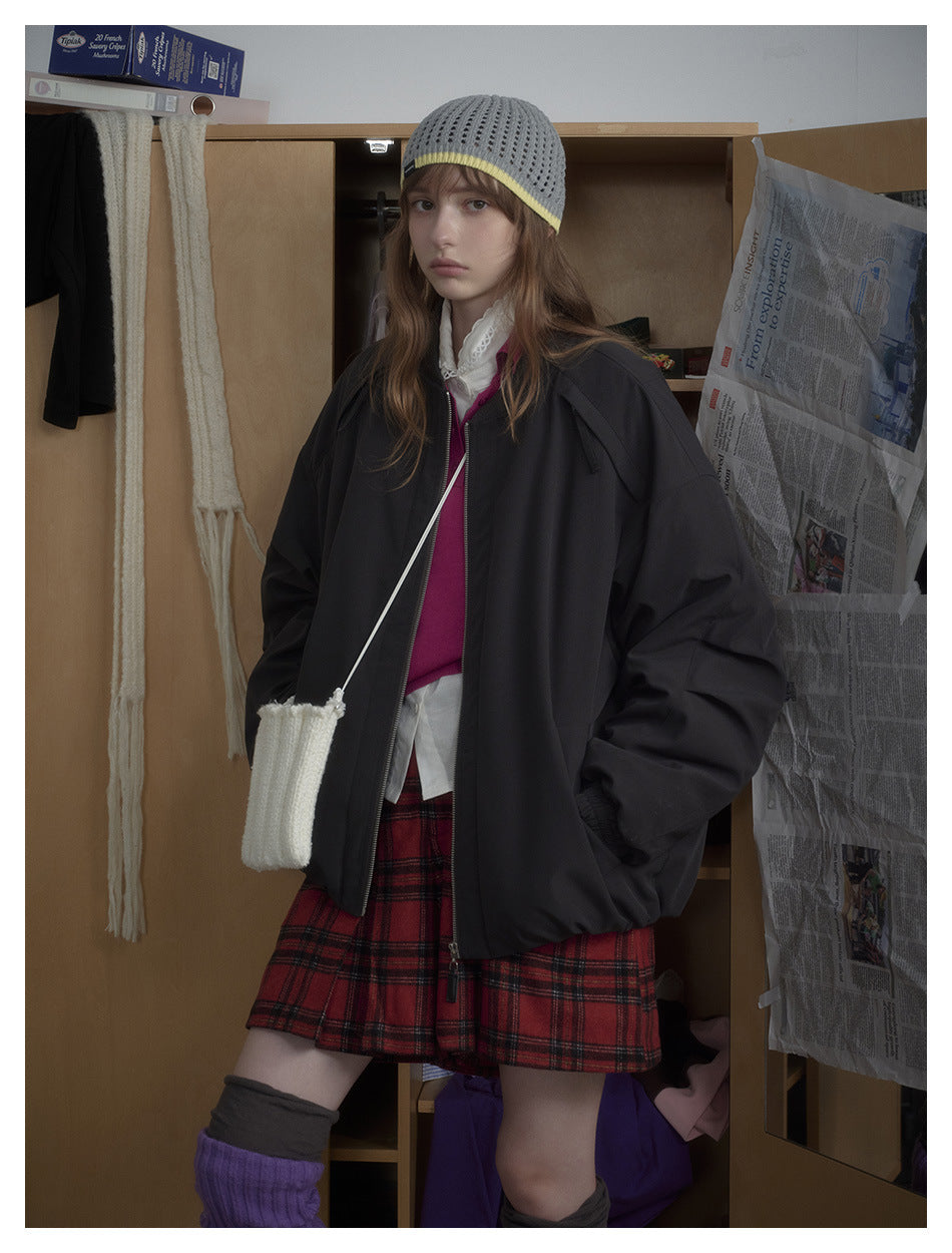 Model wearing an oversized black bomber jacket with a front zipper and gathered cuffs, paired with red plaid shorts.