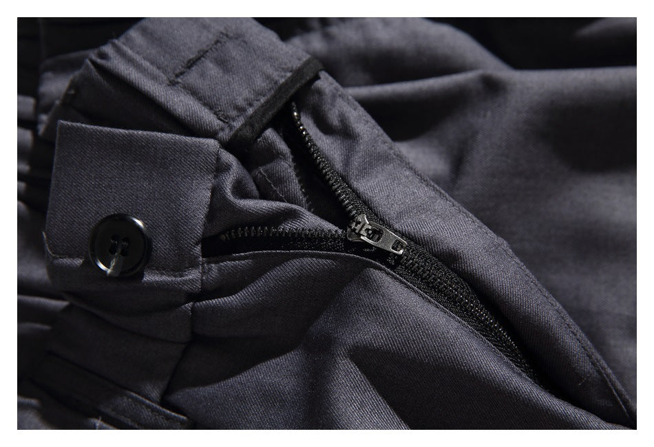 Close-up of dark charcoal trousers showing a black zipper, button tab, and stitched seams.