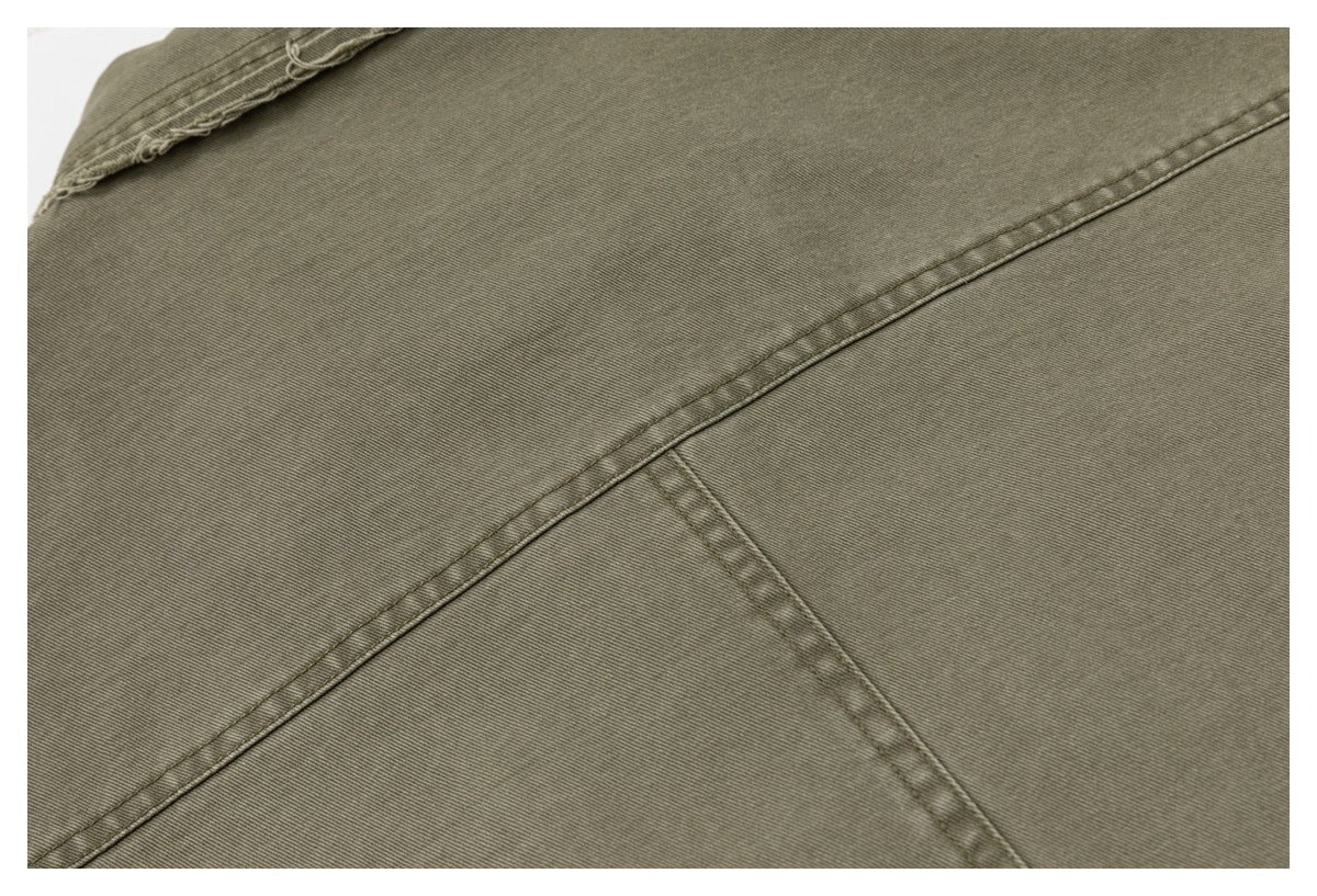 Close-up of olive-gray garment panels with diagonal and intersecting stitched seams.
