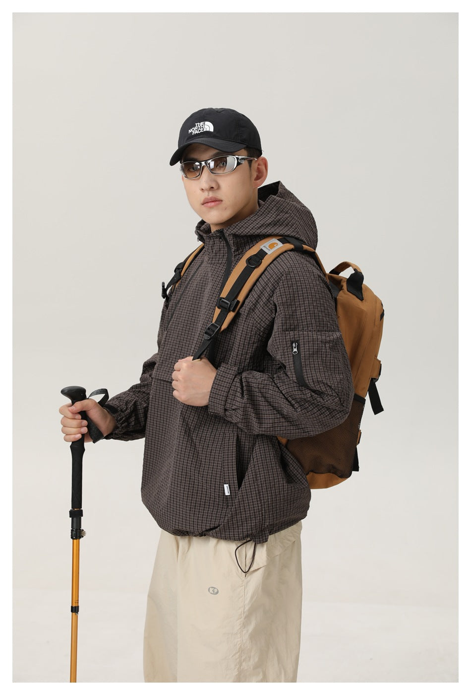 Model wearing a dark brown fine-grid hooded pullover jacket with a kangaroo pocket and zippered sleeve pocket.
