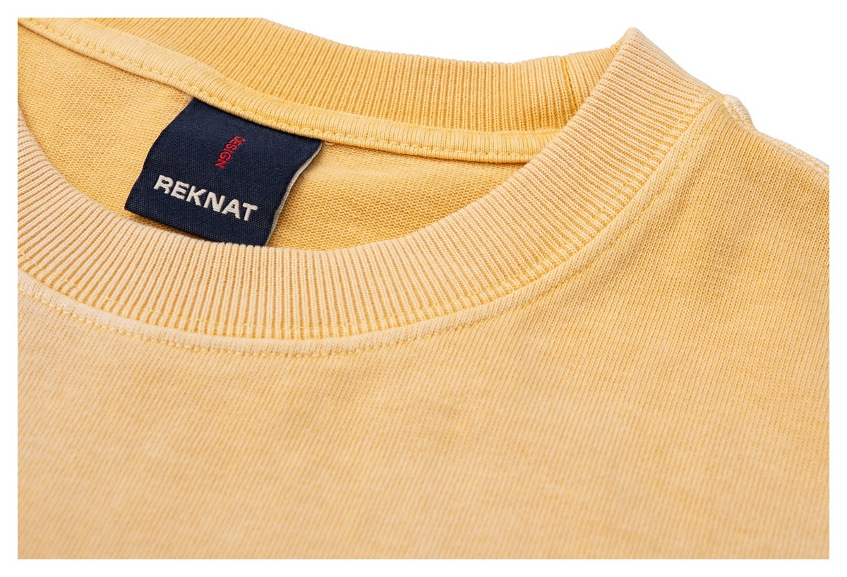 Close-up of the golden-yellow sweatshirt’s ribbed crewneck and sewn-in dark REKNAT label.