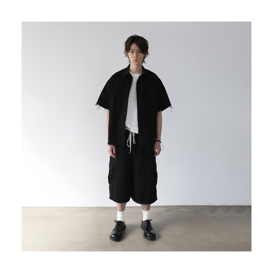 Model wearing a black short-sleeve button-up shirt with chest pockets and frayed edges, styled with a white tee and black
