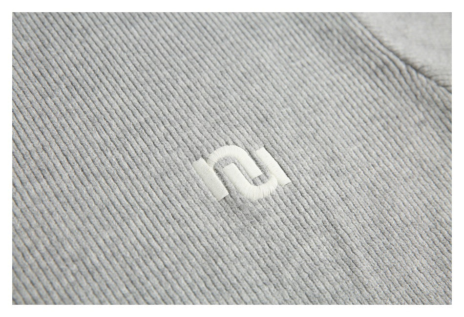 Close-up of a small white embroidered emblem on light gray ribbed knit fabric.
