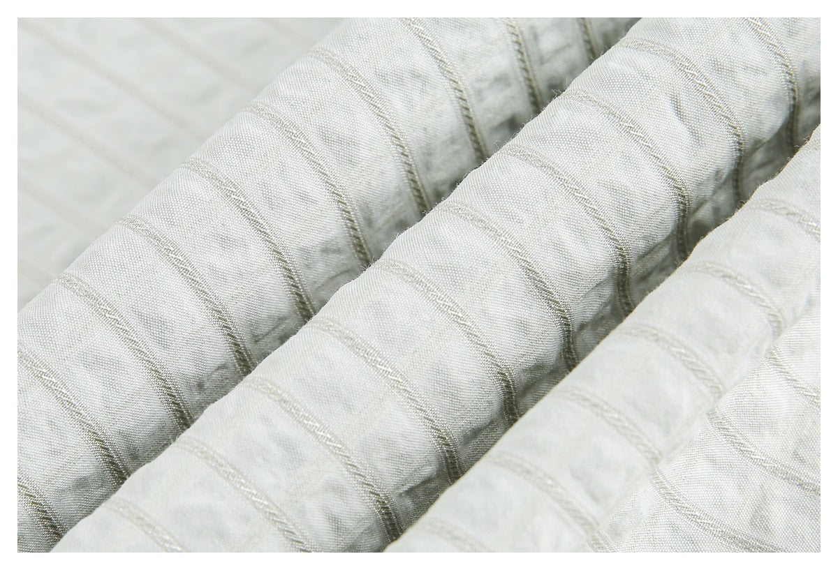 Macro view of ivory fabric with raised diagonal stripe stitching and softly gathered folds.