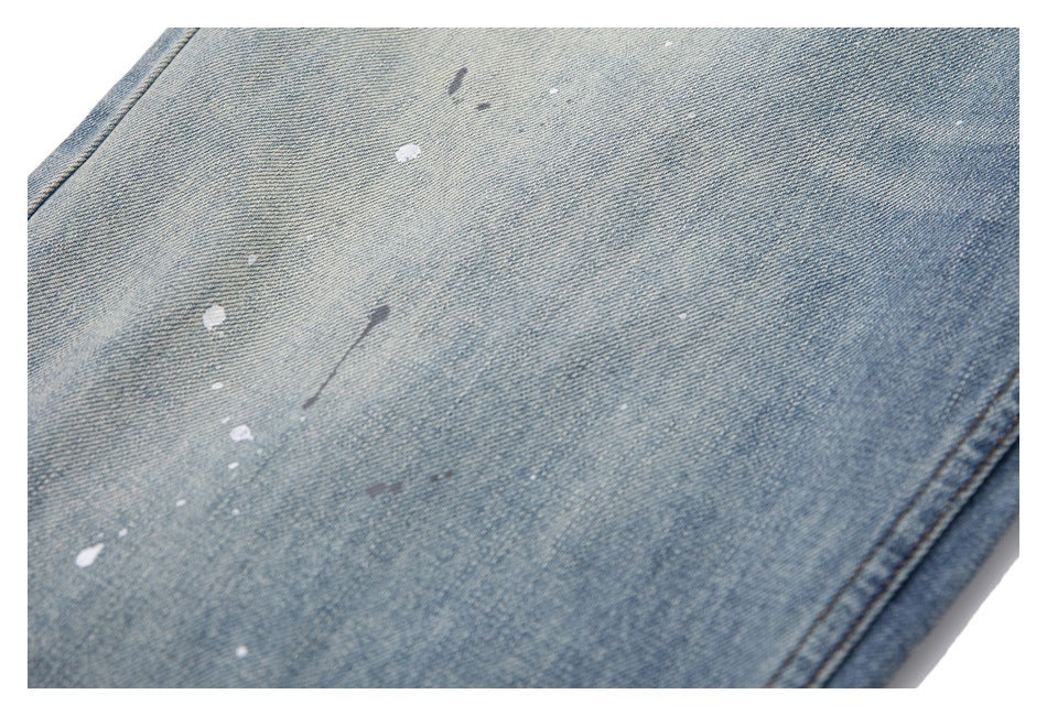 Close-up of light blue denim with scattered paint splatters and edge stitching.