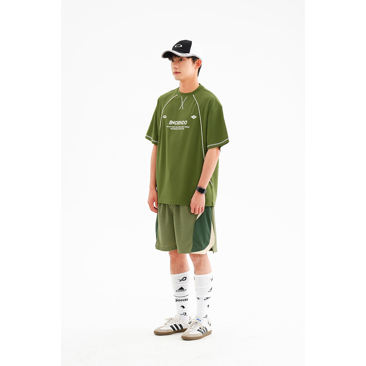 Model wearing an olive green athletic T-shirt with pale piping and matching color-block shorts, shown from the front.