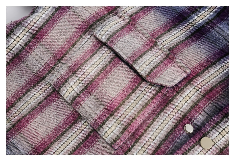 Close-up of plaid shirt fabric showing flap pockets and two metal snap buttons in pink, purple, cream, and gray.