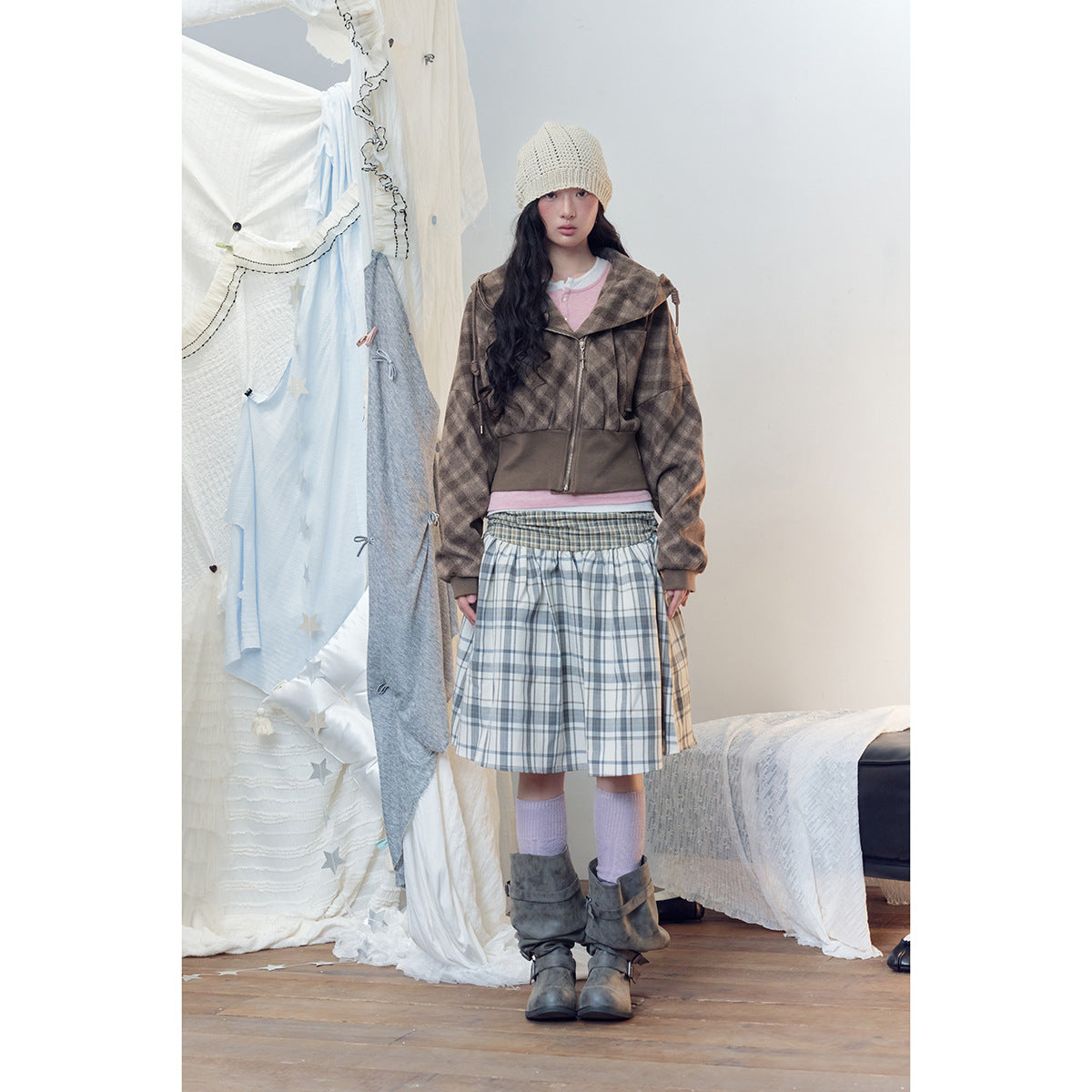 Model wears a brown plaid cropped hooded jacket, pink top, blue-gray plaid skirt, cream knit beanie and lavender socks.