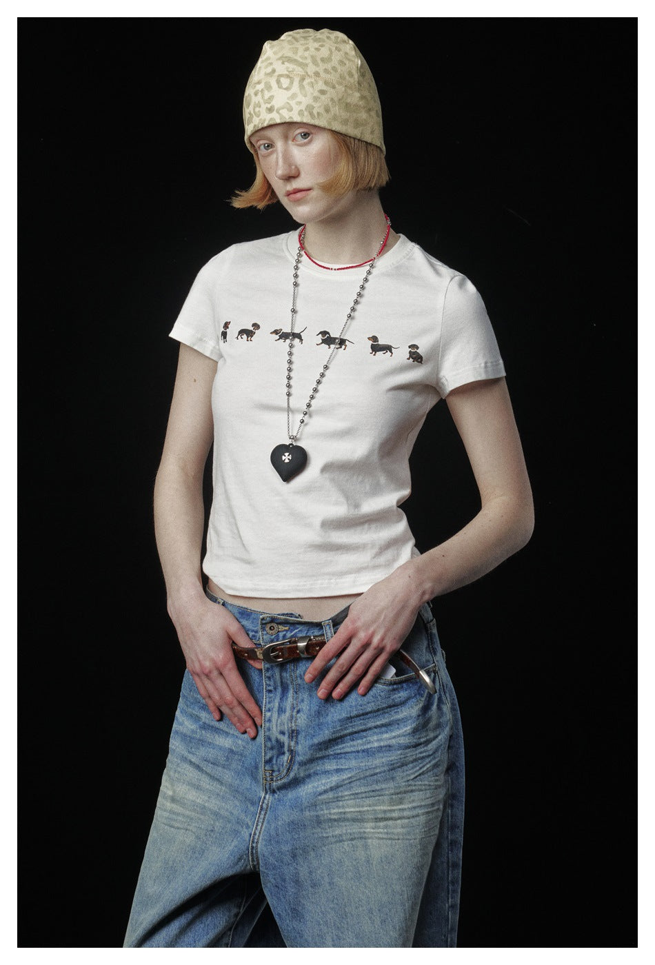 Model wearing a white short-sleeve T-shirt with a row of small dog prints, blue jeans and a beige patterned beanie.
