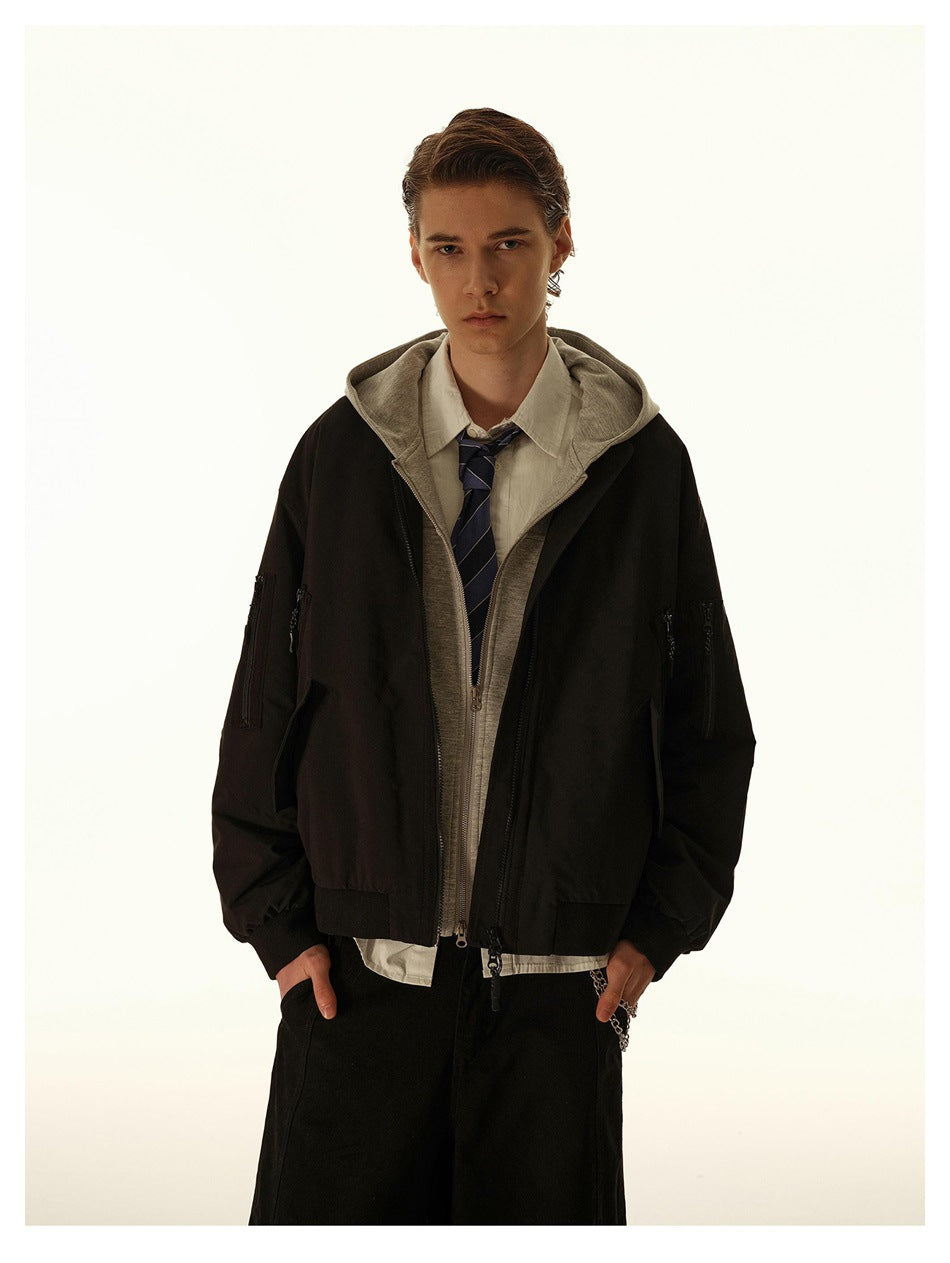 Person wearing a black bomber-style jacket open over a gray hooded layer, white shirt and striped tie