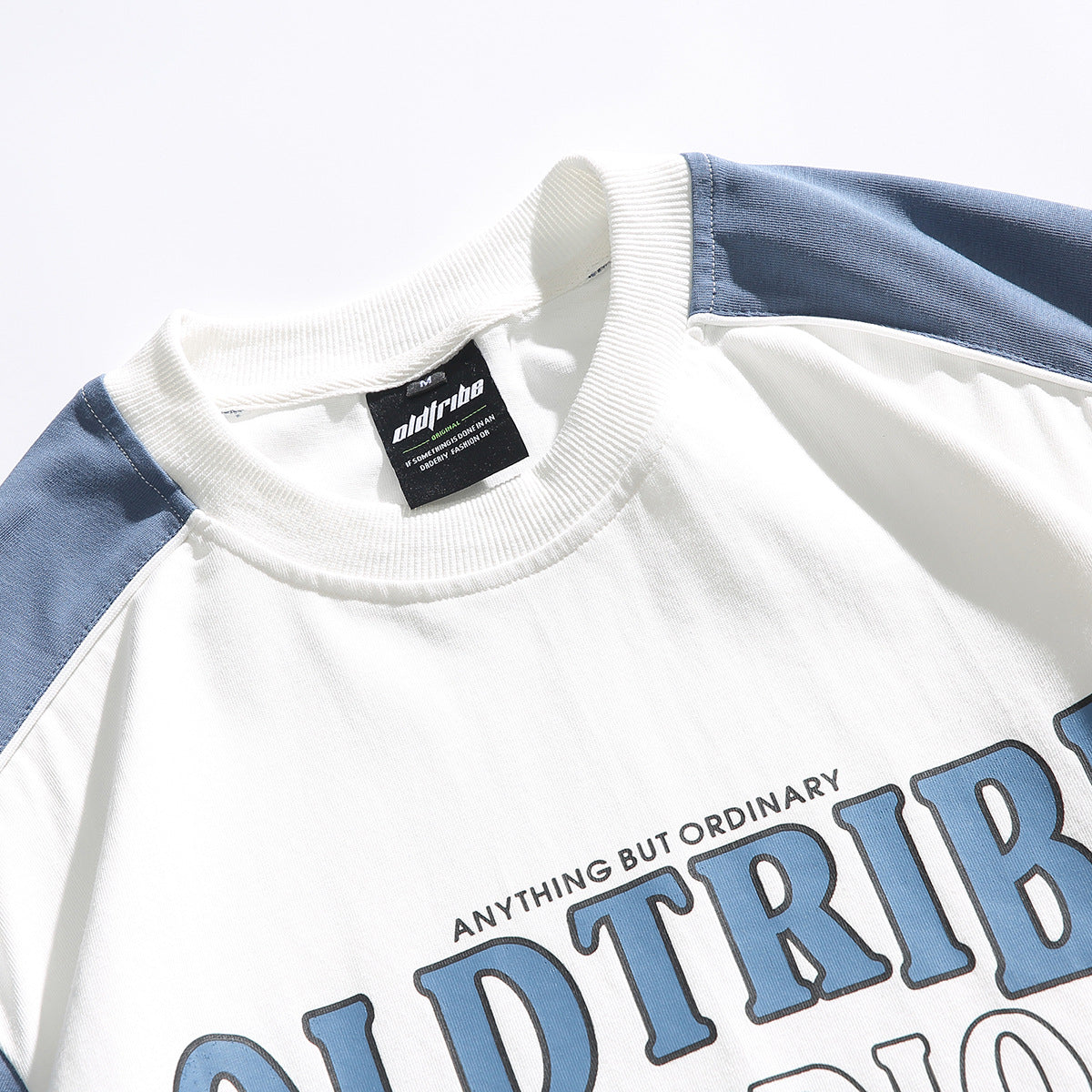 Close-up of a white crewneck shirt with blue shoulder panels, a black neck label, and part of a blue chest print.