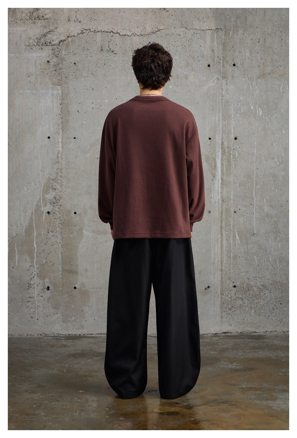 Back view of a model wearing a plain burgundy oversized sweatshirt and loose black trousers.
