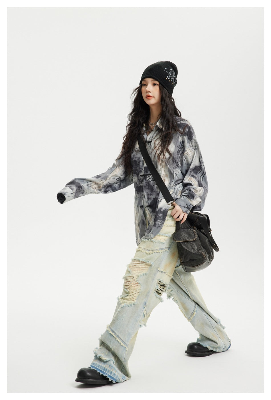 Model wearing an oversized gray abstract-print shirt with black frog closures, pale distressed jeans, and a black beanie.