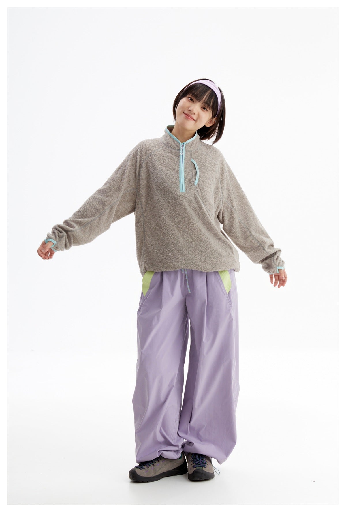 Model wearing a gray textured quarter-zip pullover with turquoise trim and loose lavender trousers.