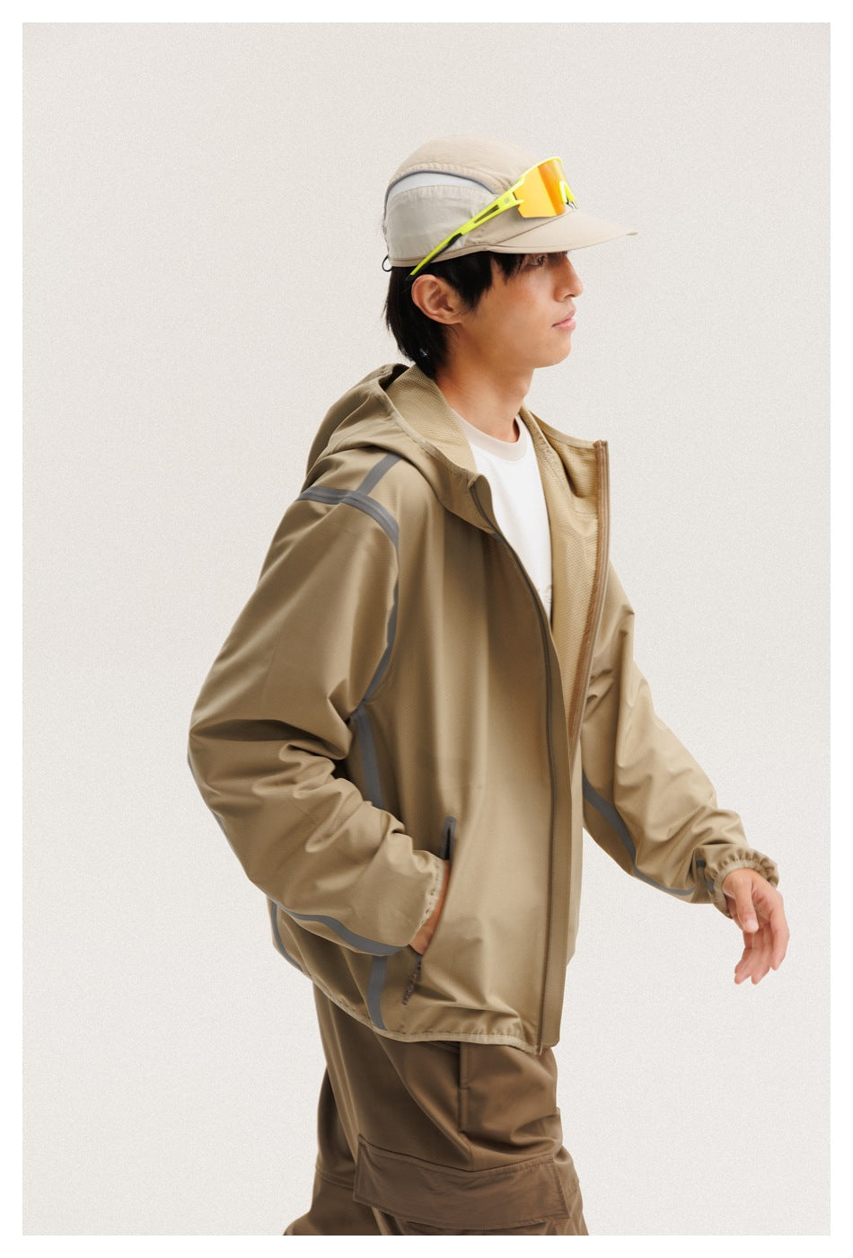 Side view of a model wearing a tan hooded zip jacket with gray trim and brown cargo pants.
