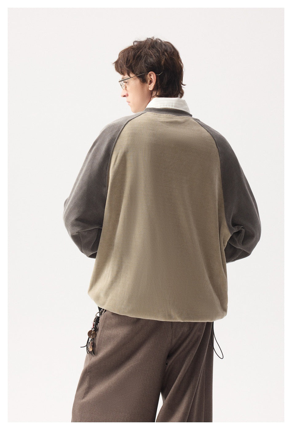Back view of a model wearing a beige pullover with gray raglan sleeves and brown trousers.