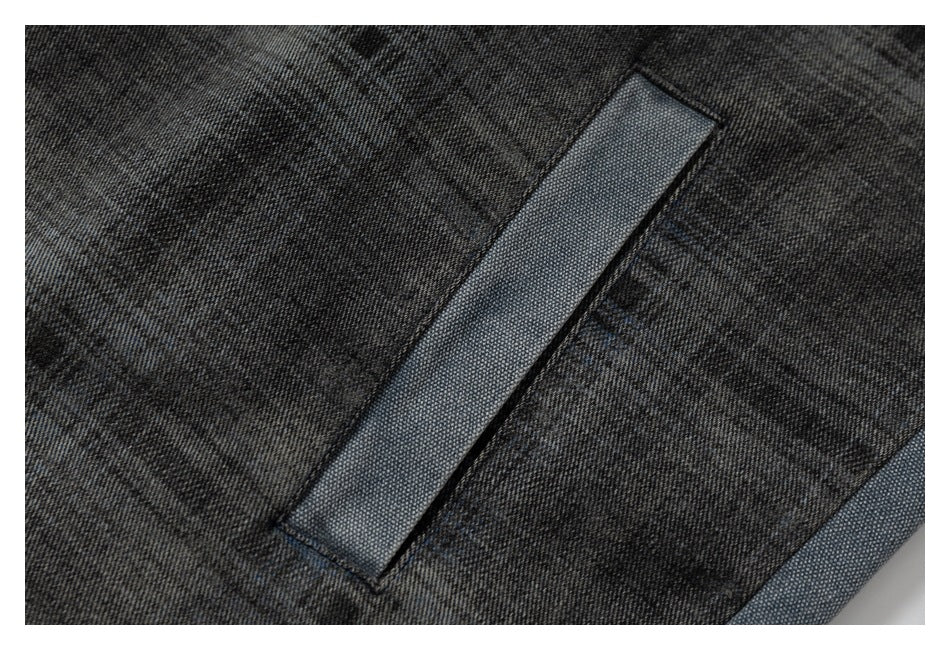 Close-up of a narrow light blue denim welt pocket set into charcoal plaid jacket fabric.