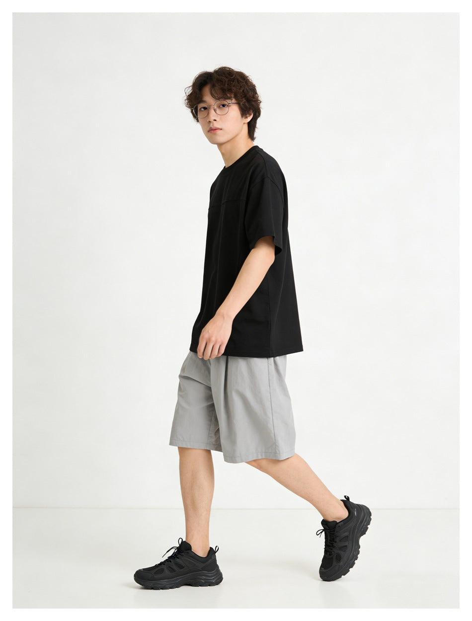 Model in a black oversized short-sleeve t-shirt with gray shorts and black sneakers, side view