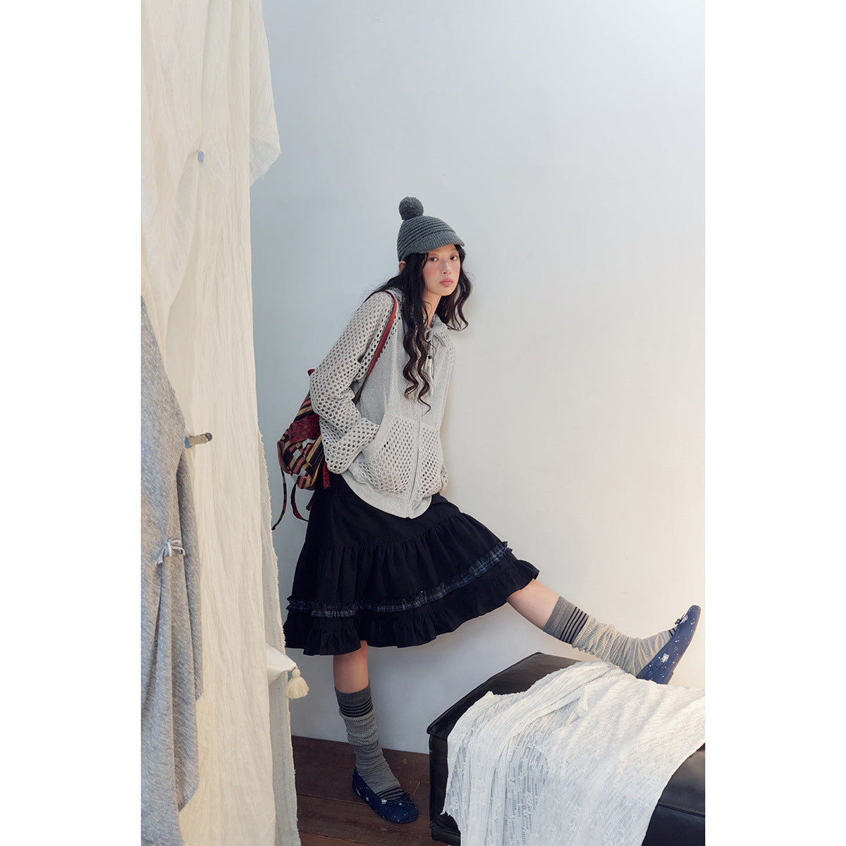 Side view of a model wearing a light gray open-knit sleeve hoodie and a navy tiered ruffle skirt.