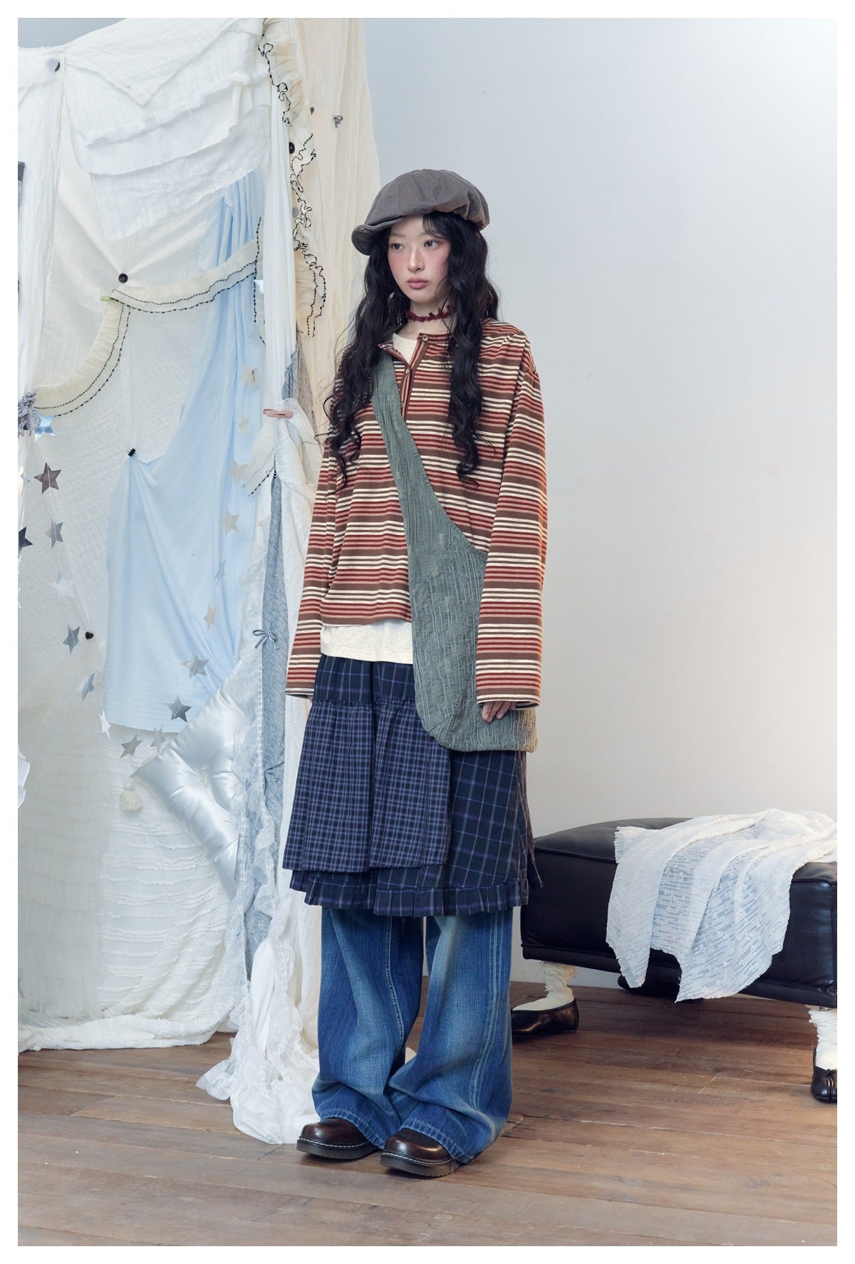 Model shown standing in a rust-and-cream striped henley, layered navy plaid skirt and wide-leg blue jeans.