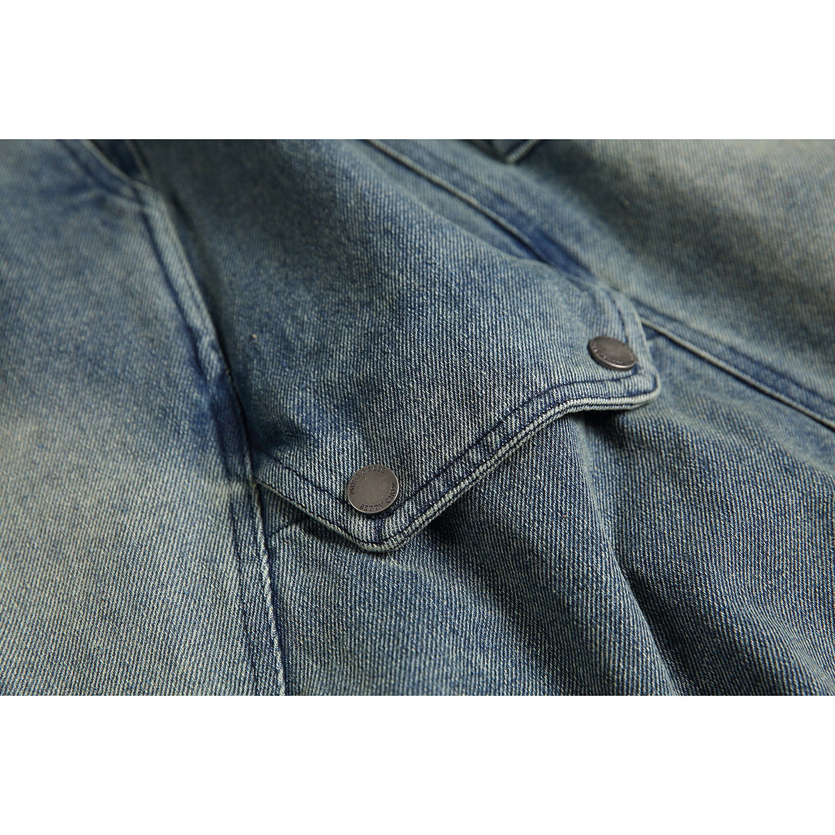 Close-up of a buttoned flap pocket and stitching on blue-gray denim shorts.