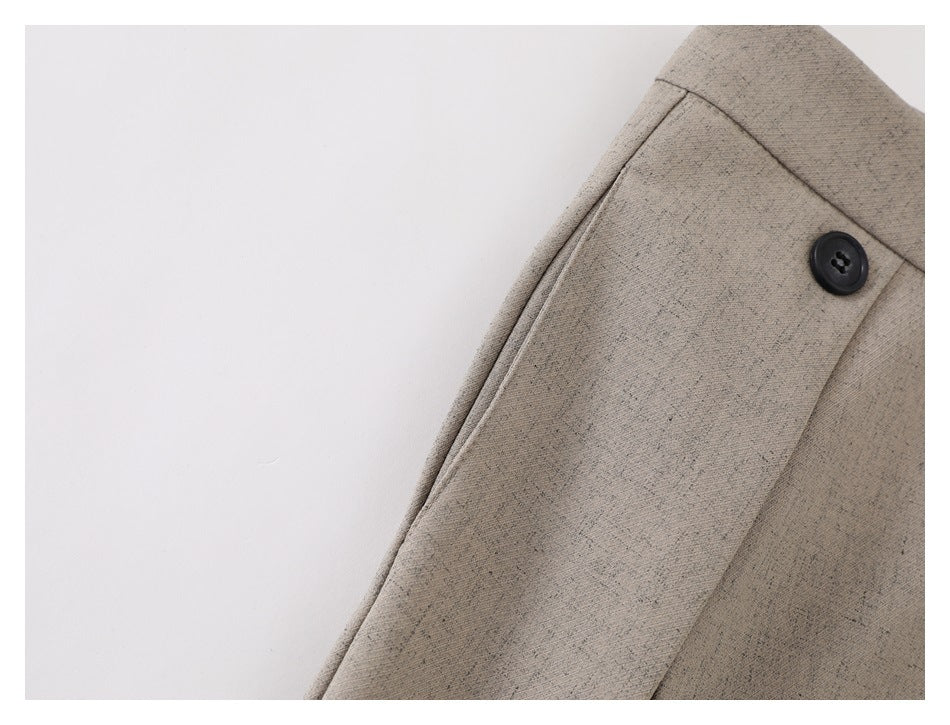 Close-up of taupe trousers showing a black button beside the stitched front waistband panel.