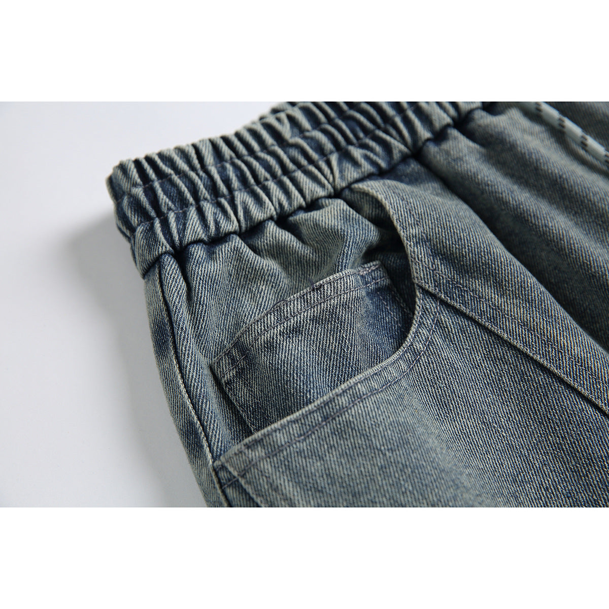 Close-up of the gray-blue denim shorts' gathered elastic waistband and curved pocket opening.