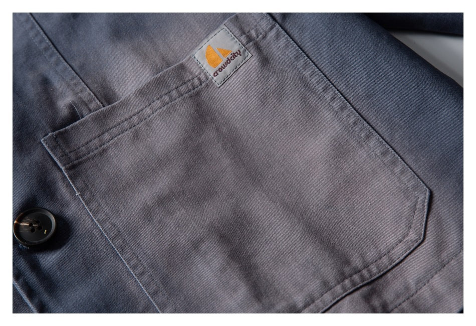 Close-up of a gray jacket’s large patch pocket and small sewn-on logo tab.