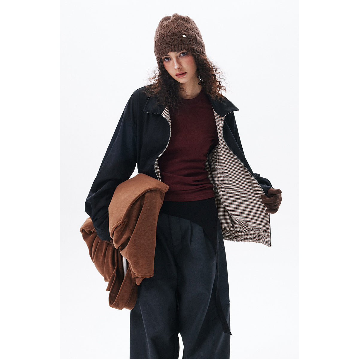 Model wearing an open dark navy jacket with beige-and-brown checked lining, navy trousers, and a brown knit beanie.