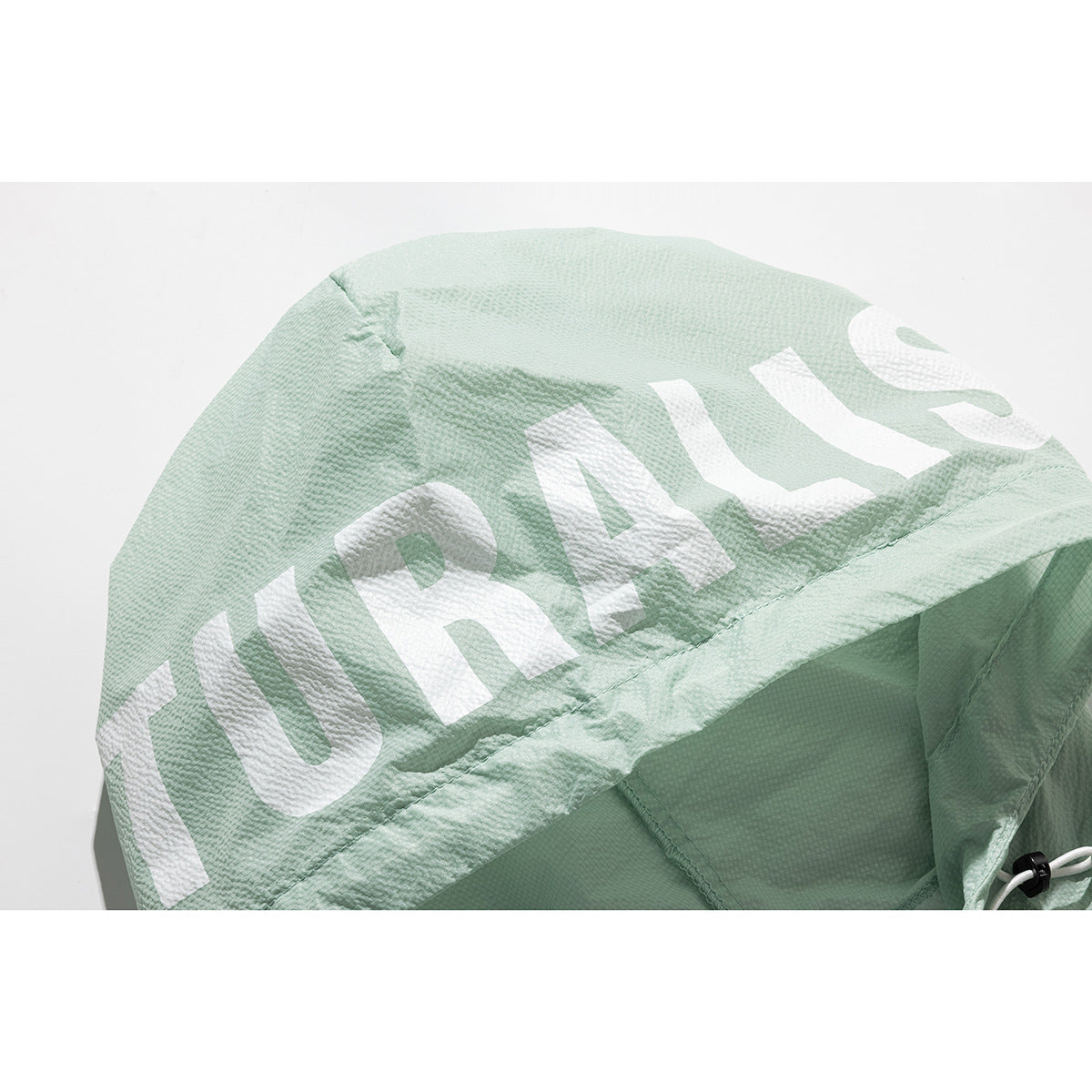 Close-up of a pale mint jacket hood with large white lettering and an adjustable drawcord.