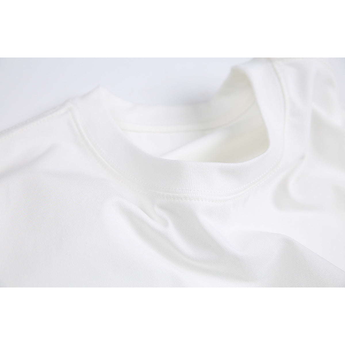 Close-up of the white T-shirt’s ribbed crew neckline and stitching.
