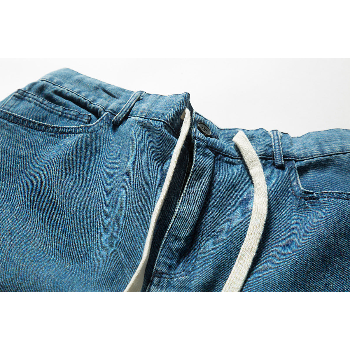 Close-up of blue denim shorts showing the front waistband, button, belt loops, pockets and white drawstrings.