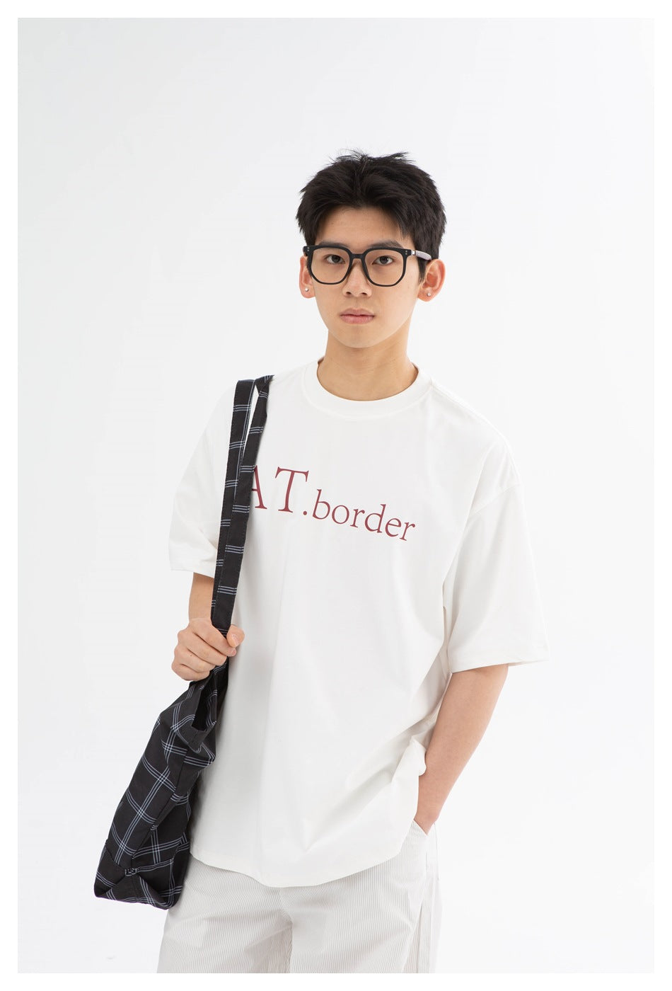 Front view of a model wearing a white oversized graphic T-shirt with burgundy lettering and a black plaid shoulder bag.