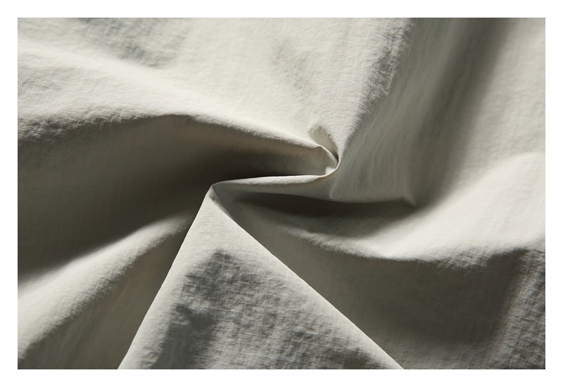 Close-up of pale gray, subtly crinkled woven fabric draped into soft folds.