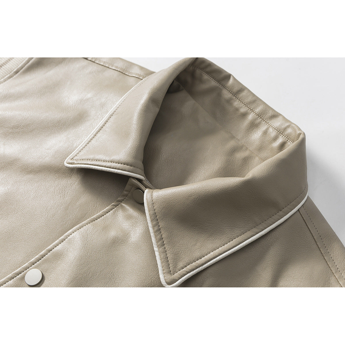 Close-up of a light taupe jacket collar with pale piping and a matching snap button.
