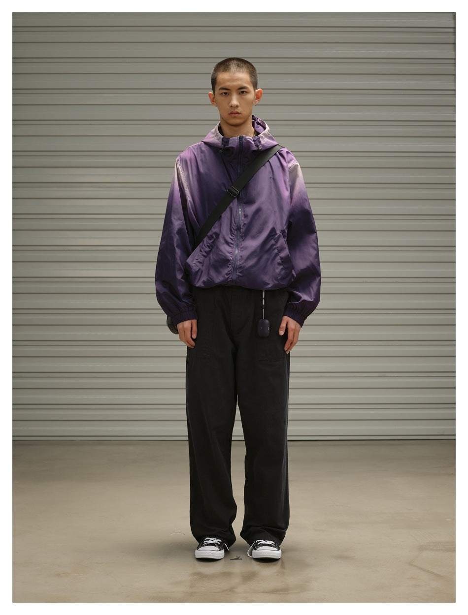 Man wearing a purple hooded zip jacket with elastic cuffs, black trousers and a black crossbody bag.