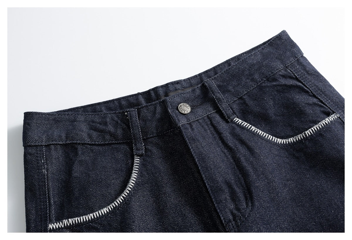 Close-up of dark indigo denim trousers showing the waistband, metal button, fly and curved front pockets with white